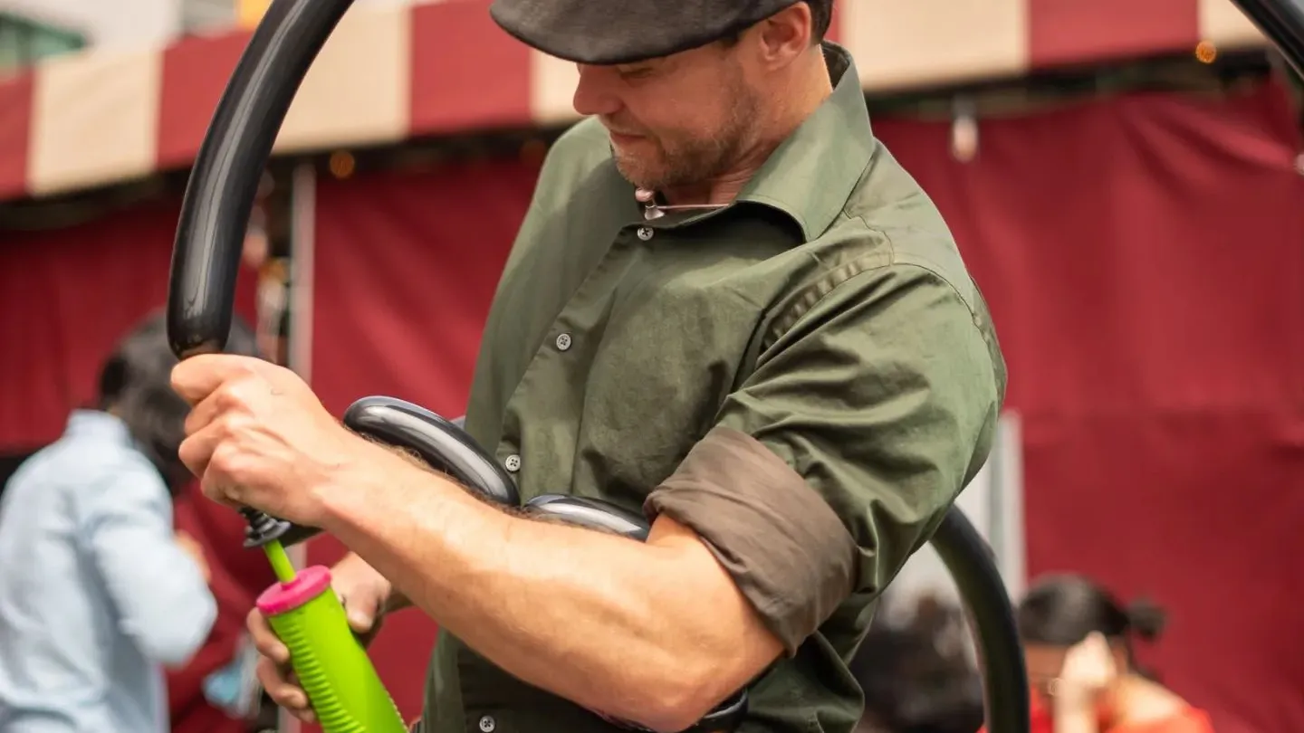 a man wearing a hat blowing animal balloons