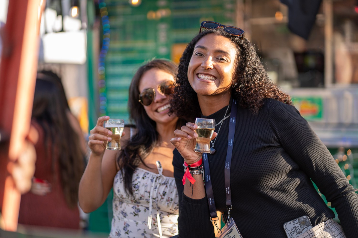 Two women smiling and holding drinks at an outdoor event.