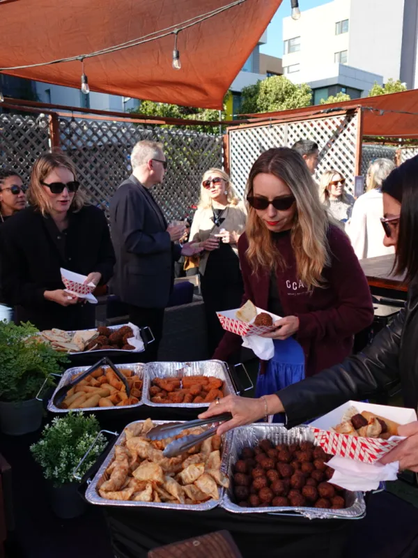 People serving food from trays at an outdoor event with trays of appetizers.