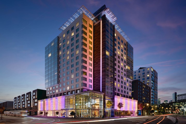 Tall modern building with purple lighting at dusk, city street view.